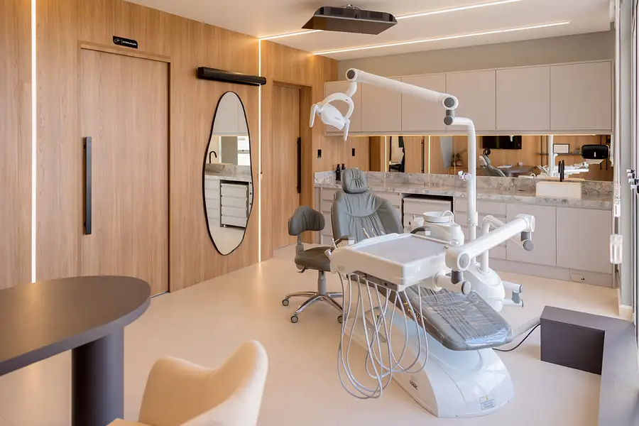 Cadeira odontológica ao lado de espelho orgânico e painel de madeira